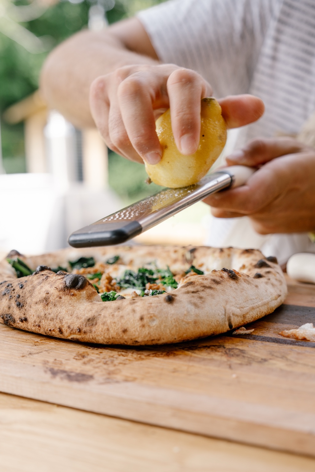 Finishing a wood-fired pizza with fresh lemon zest
